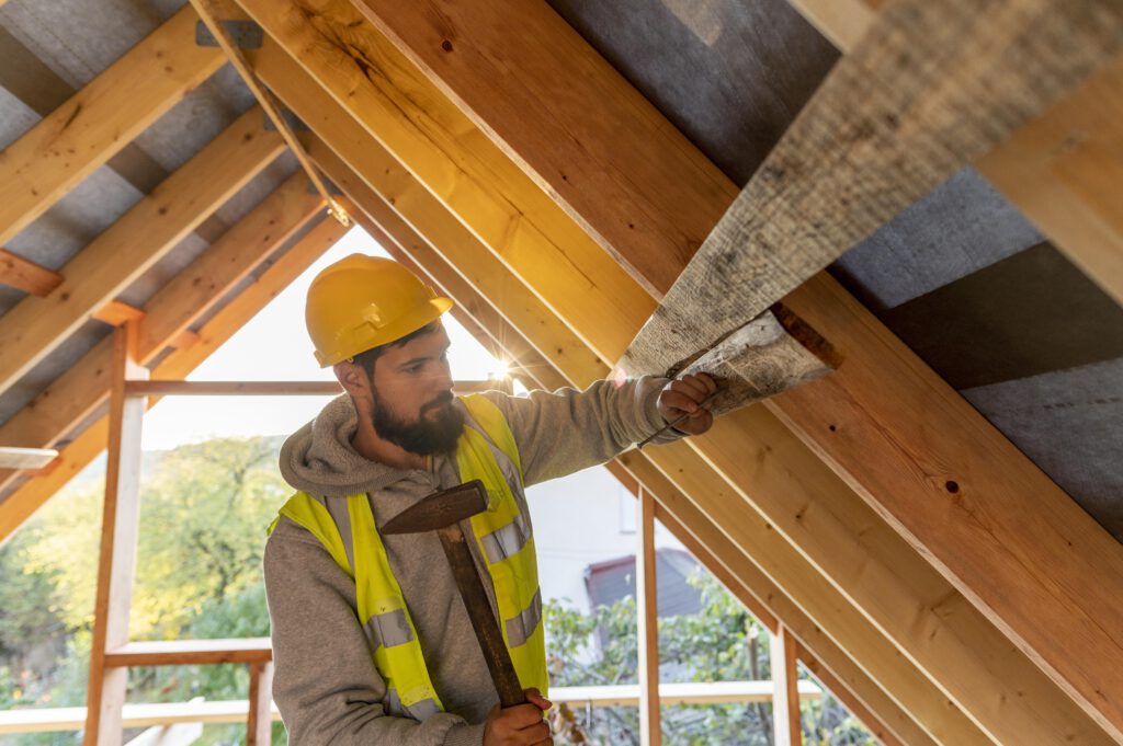 Handwerker befestigt Dämmmaterial zwischen den Sparren eines offenen Dachstuhls, um die Energieeffizienz zu erhöhen.