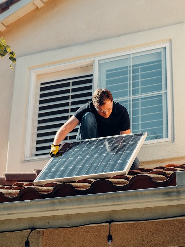 Installateur montiert Solarmodul auf dem Dach eines Hauses um mit nachhaltiger Energie und mit Photovoltaik CO2-Emissionen reduzieren