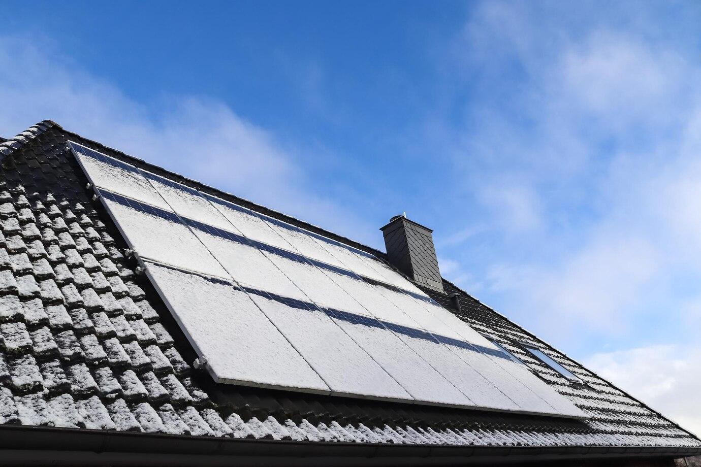 Dach eines Einfamilienhauses mit teilweise schneebedeckten Solarmodulen unter blauem Himmel.